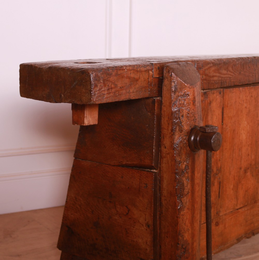 A rustic French primitive timber workbench with an integrated wooden vice mechanism and a thick slab top. View II