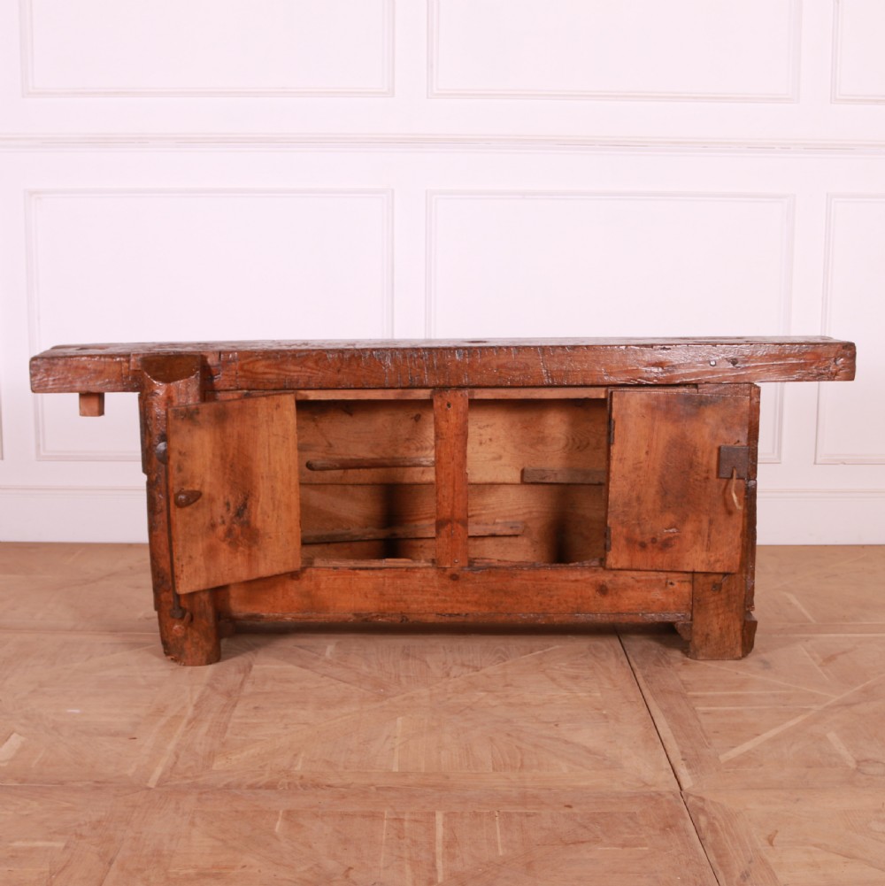 A rustic French primitive timber workbench with an integrated wooden vice mechanism and a thick slab top. View V