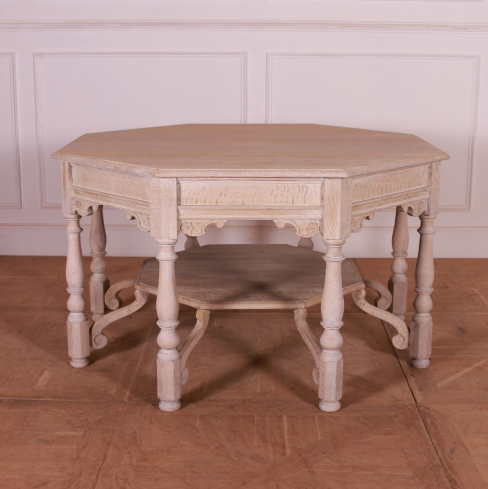 An octagonal bleached oak centre table featuring turned legs, a lower shelf, and decorative carved aprons.