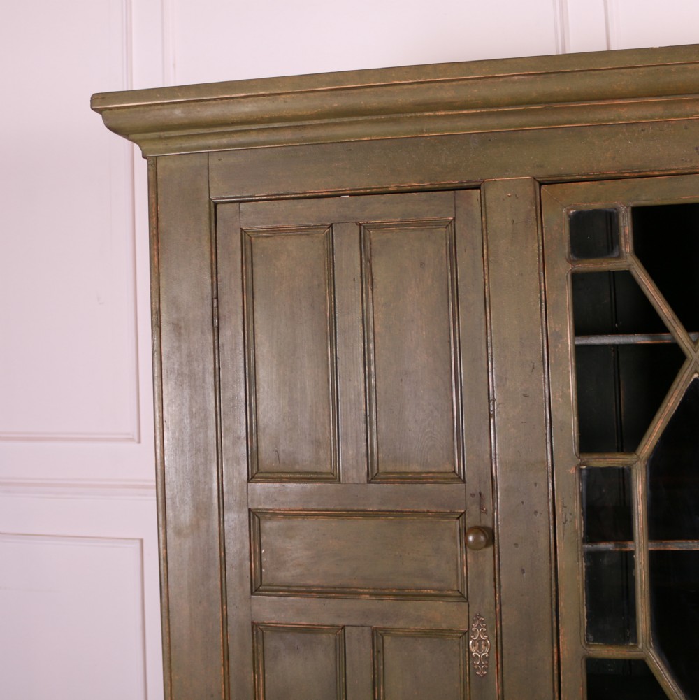 A large green painted pine cupboard featuring a central glazed door with geometric glazing bars flanked by two panelled doors above five drawers. View II