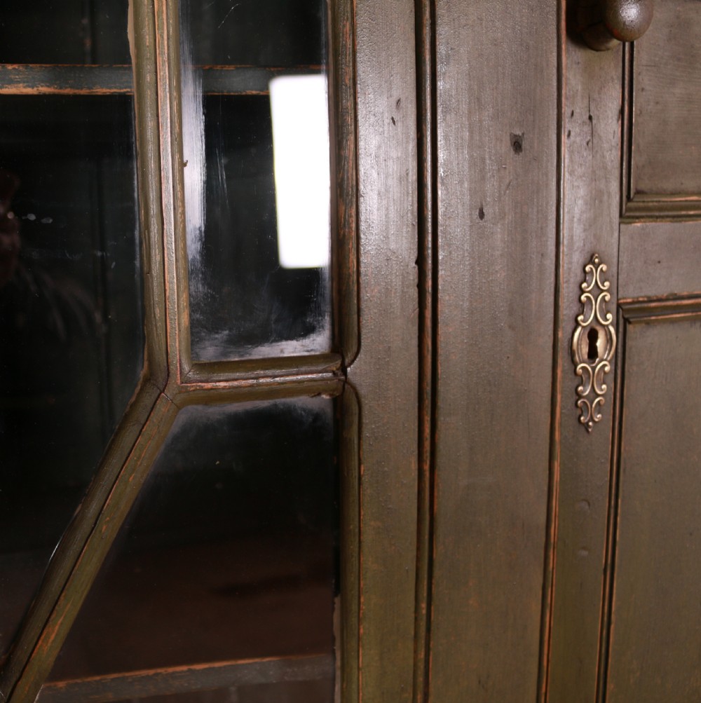 A large green painted pine cupboard featuring a central glazed door with geometric glazing bars flanked by two panelled doors above five drawers. View IV