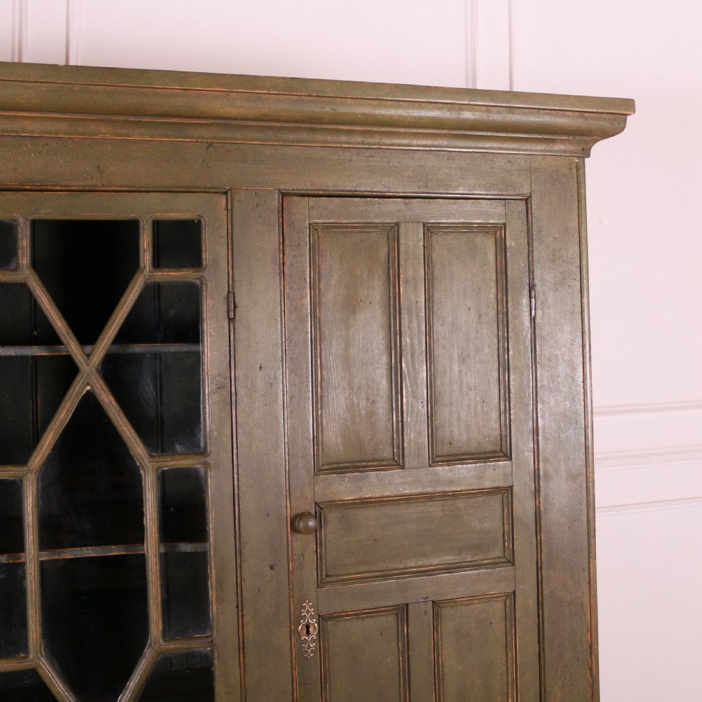 A large green painted pine cupboard featuring a central glazed door with geometric glazing bars flanked by two panelled doors above five drawers. View V