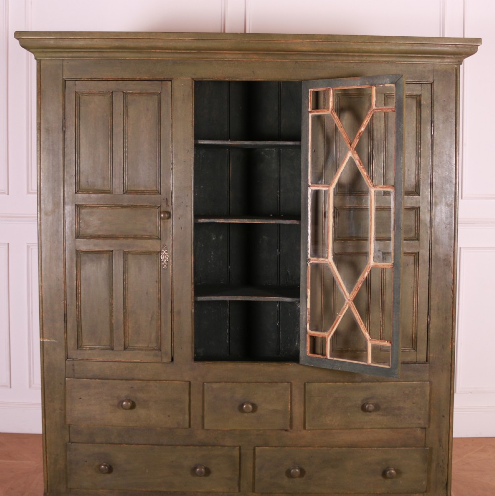 A large green painted pine cupboard featuring a central glazed door with geometric glazing bars flanked by two panelled doors above five drawers. View VIII