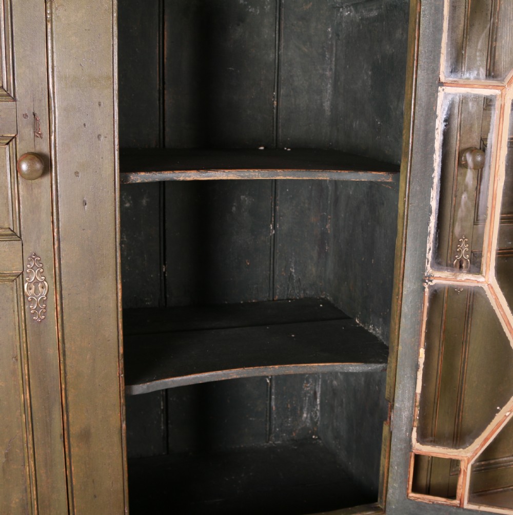 A large green painted pine cupboard featuring a central glazed door with geometric glazing bars flanked by two panelled doors above five drawers. View IX