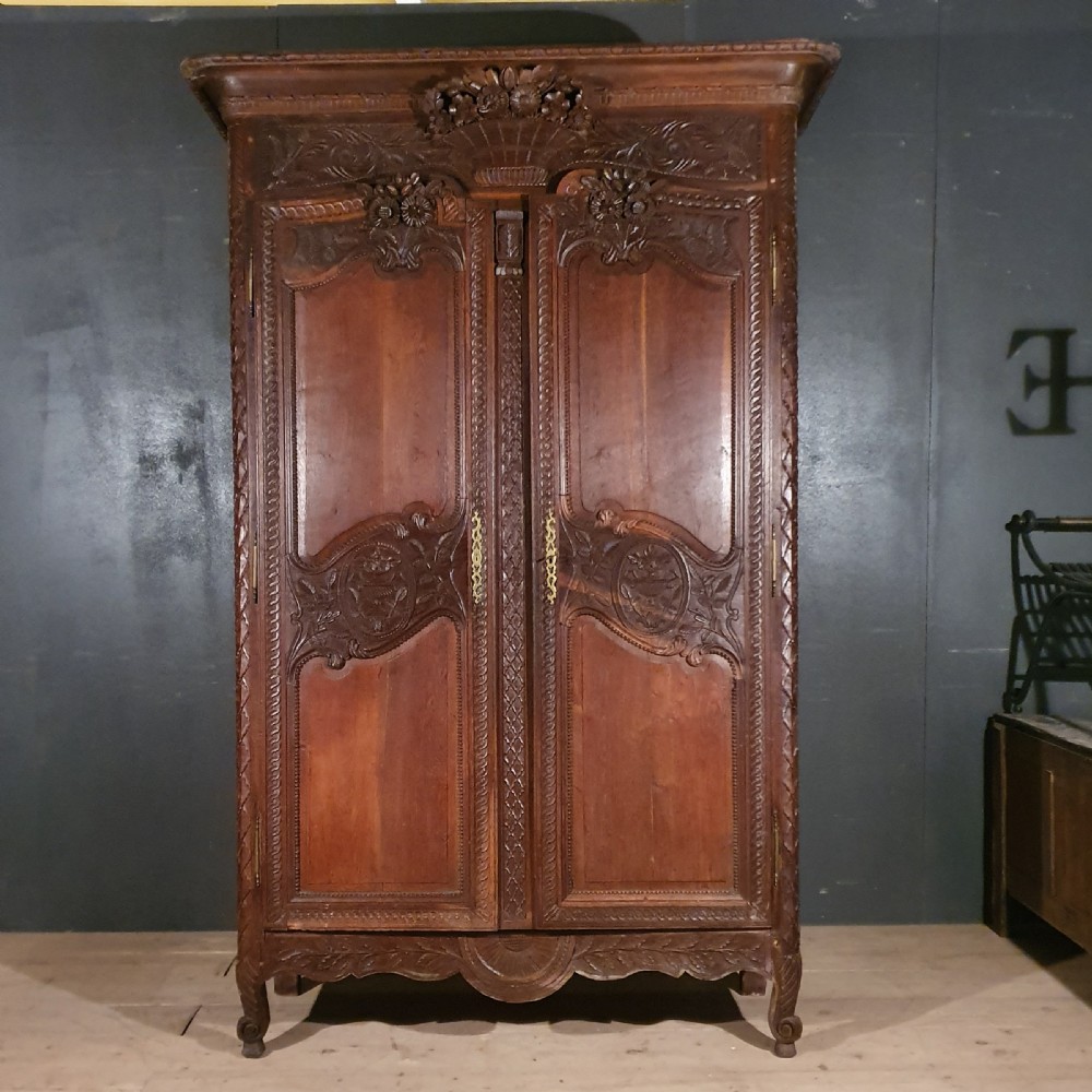 A tall French oak armoire featuring two arched double doors adorned with detailed floral carvings and standing on short cabriole feet.