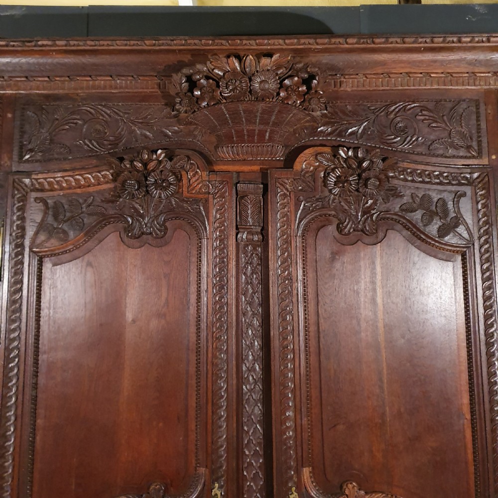 A tall French oak armoire featuring two arched double doors adorned with detailed floral carvings and standing on short cabriole feet. View III