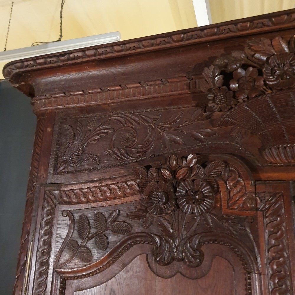 A tall French oak armoire featuring two arched double doors adorned with detailed floral carvings and standing on short cabriole feet. View IV