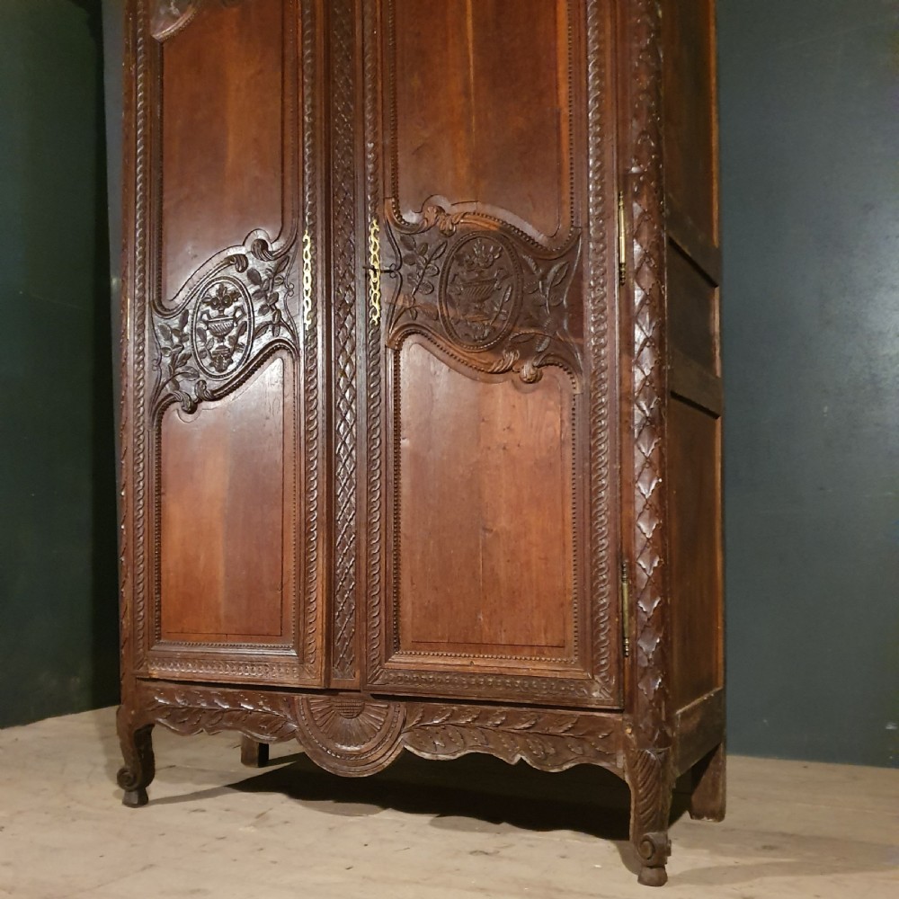 A tall French oak armoire featuring two arched double doors adorned with detailed floral carvings and standing on short cabriole feet. View VII