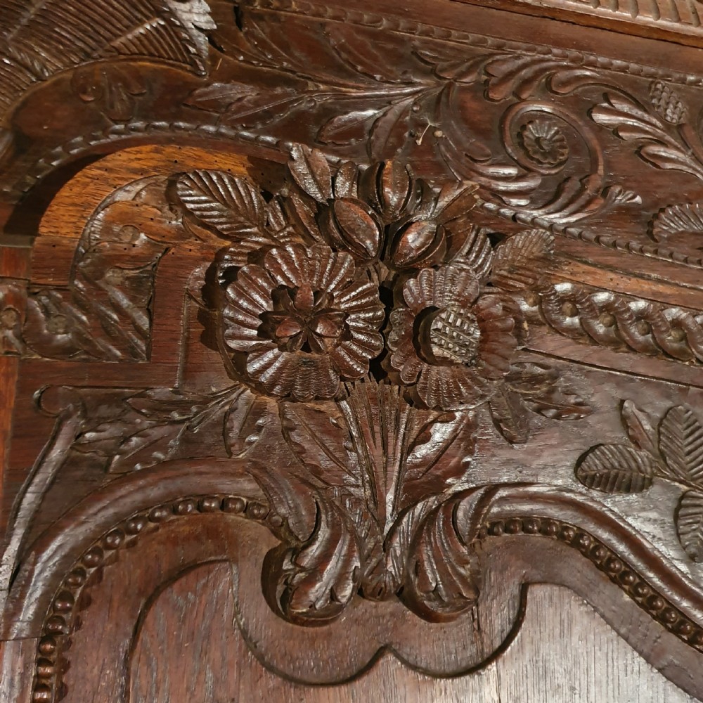 A tall French oak armoire featuring two arched double doors adorned with detailed floral carvings and standing on short cabriole feet. View IX