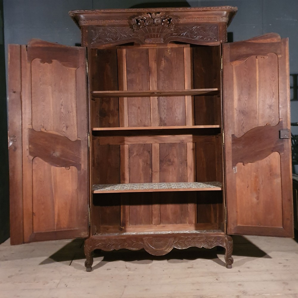 A tall French oak armoire featuring two arched double doors adorned with detailed floral carvings and standing on short cabriole feet. View X