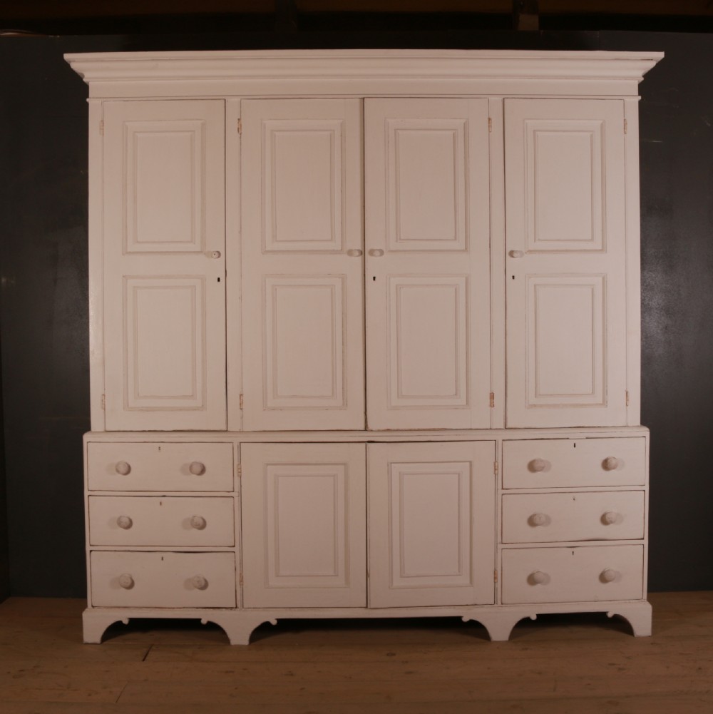 A large two-part off-white painted pine housekeepers cupboard with four upper fielded panel doors, six flanking drawers, and two central lower cabinet doors.