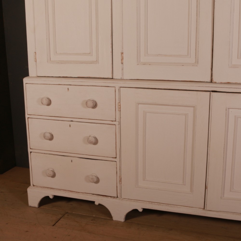 A large two-part off-white painted pine housekeepers cupboard with four upper fielded panel doors, six flanking drawers, and two central lower cabinet doors. View II
