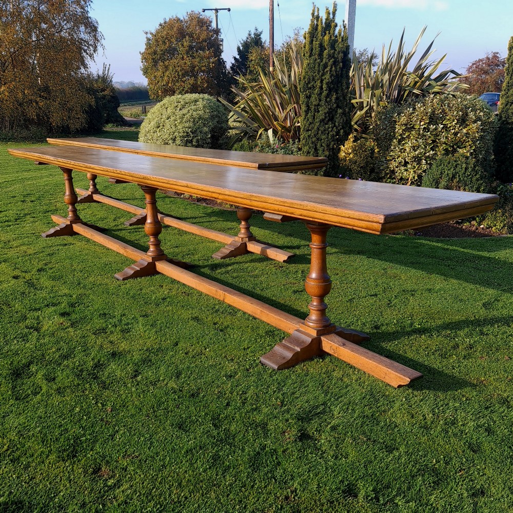 A pair of long English oak trestle dining tables featuring turned baluster supports, sturdy floor stretchers, and rectangular timber tops.