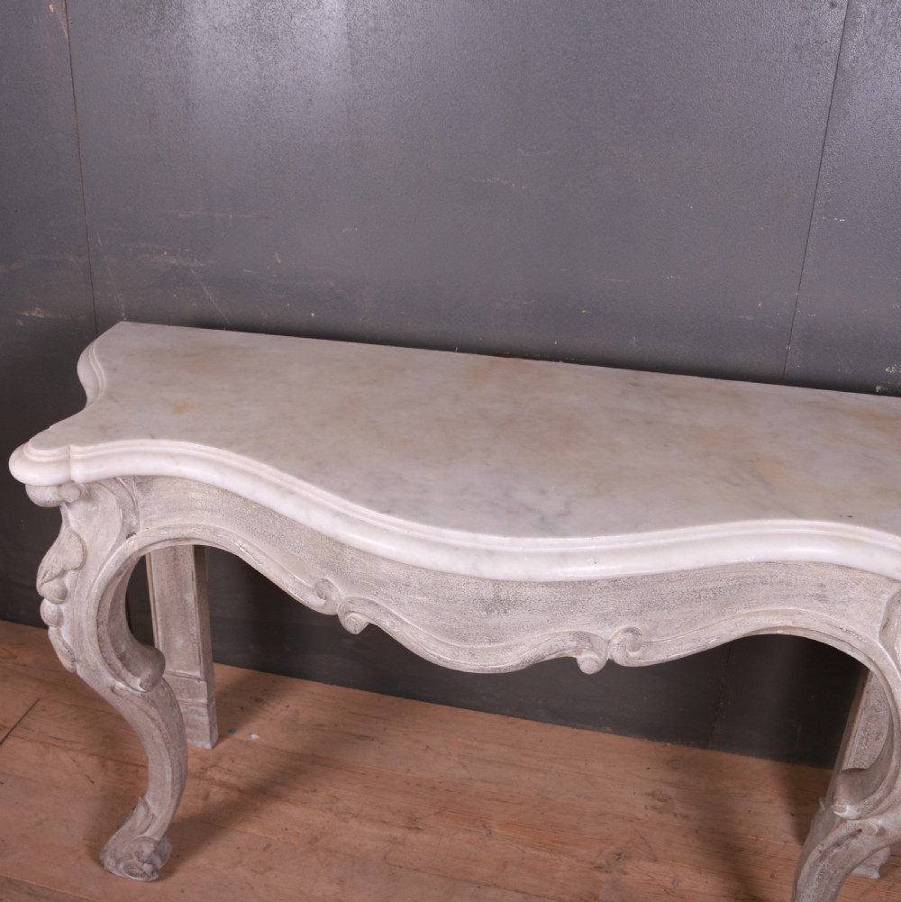 An off-white carved wooden console table with a serpentine white marble top and cabriole legs. View VII