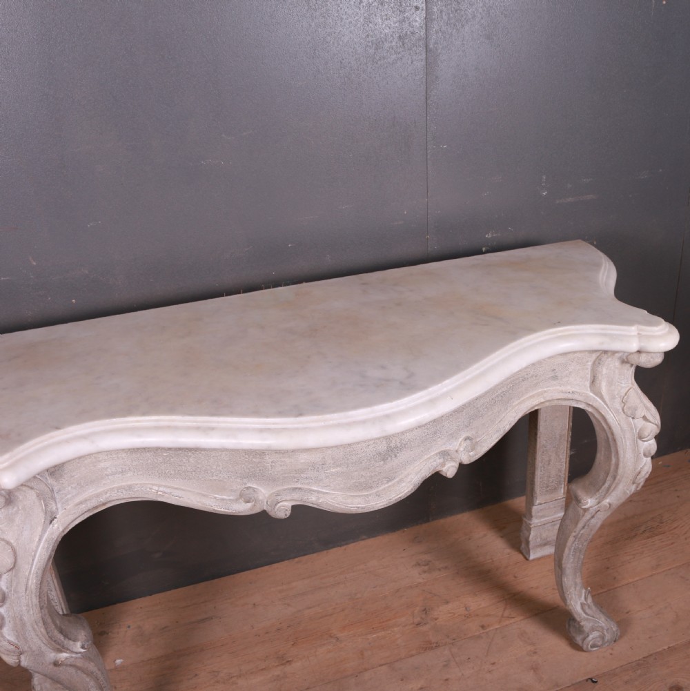 An off-white carved wooden console table with a serpentine white marble top and cabriole legs. View VIII