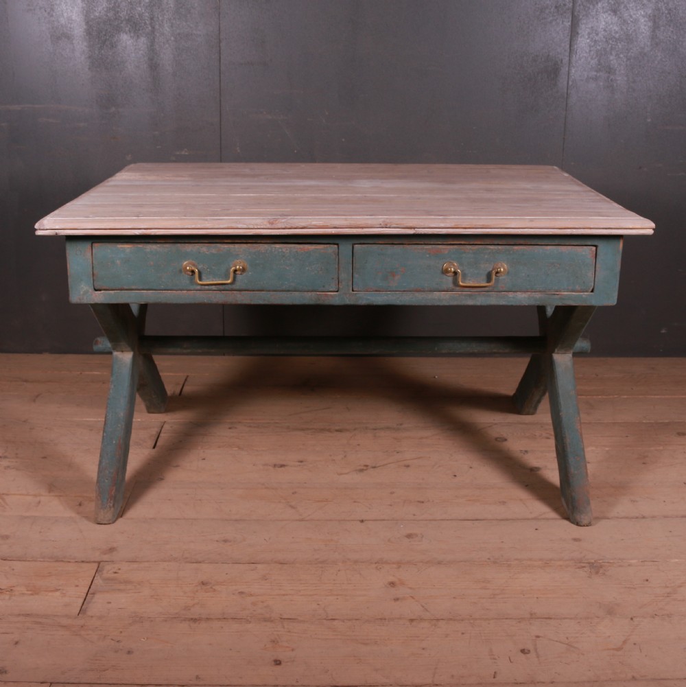 An antique English trestle table featuring a muted teal painted X-frame base, two apron drawers with brass handles, and a scrubbed natural pine top. View II