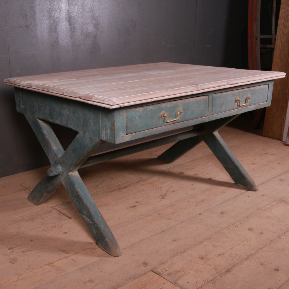 An antique English trestle table featuring a muted teal painted X-frame base, two apron drawers with brass handles, and a scrubbed natural pine top. View III