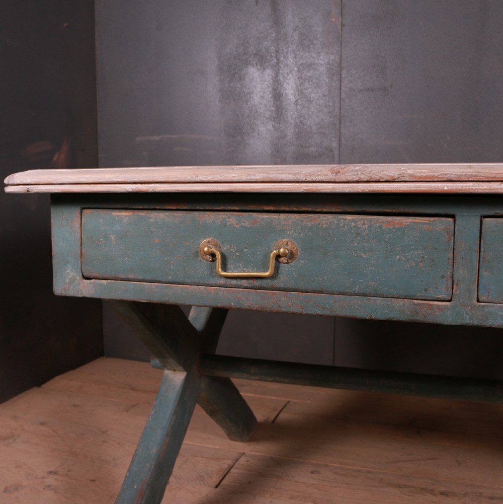 An antique English trestle table featuring a muted teal painted X-frame base, two apron drawers with brass handles, and a scrubbed natural pine top. View IV