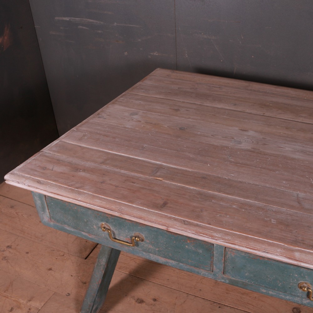 An antique English trestle table featuring a muted teal painted X-frame base, two apron drawers with brass handles, and a scrubbed natural pine top. View VIII