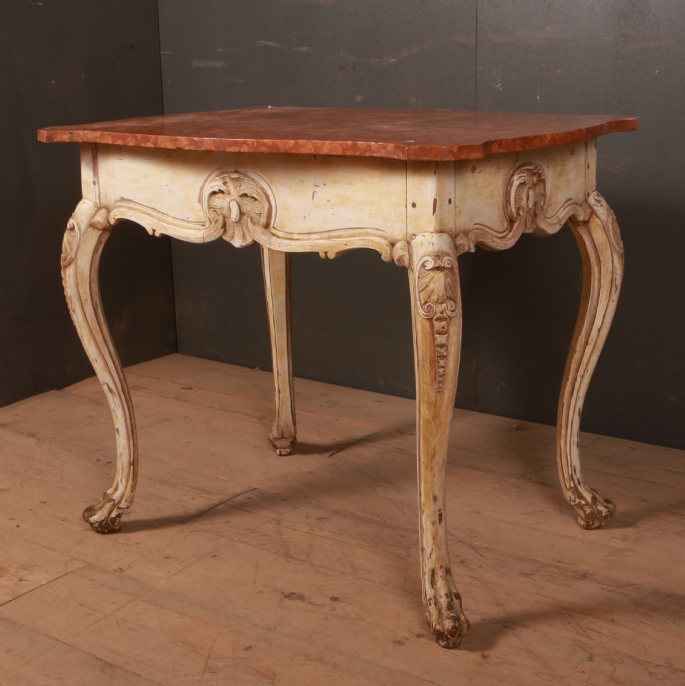 A Swedish Rococo style centre table featuring cream painted cabriole legs, carved apron motifs, and a reddish-brown marbled top.