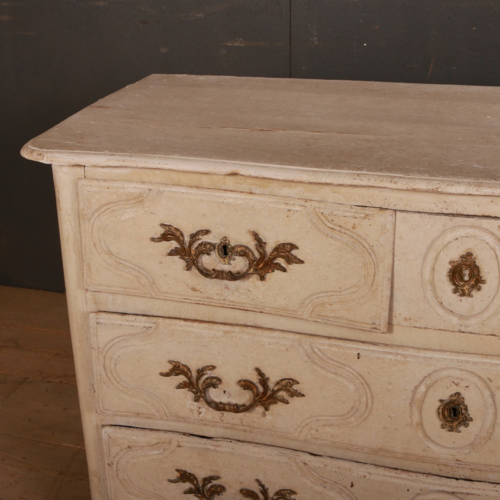 An off-white painted wooden French commode featuring three drawers with ornamental brass handles and a scalloped bottom apron. View II