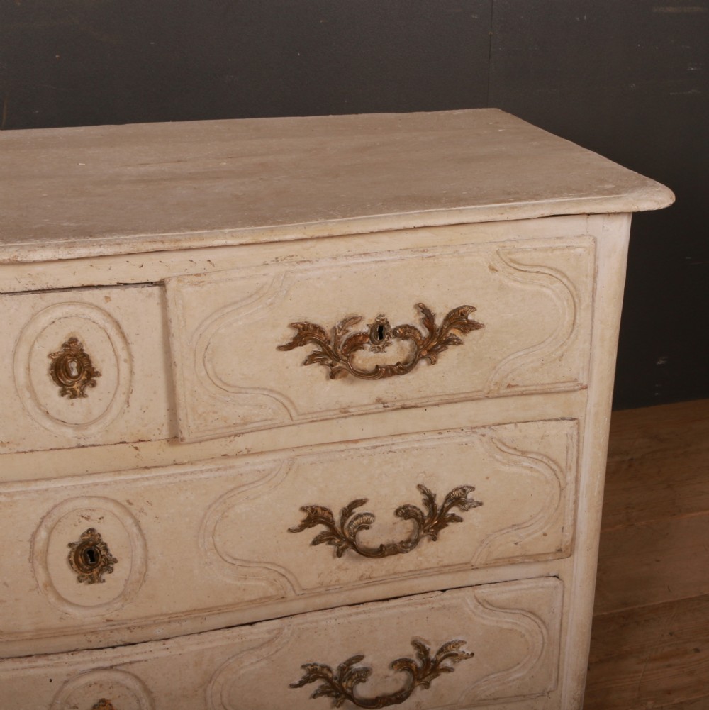 An off-white painted wooden French commode featuring three drawers with ornamental brass handles and a scalloped bottom apron. View III