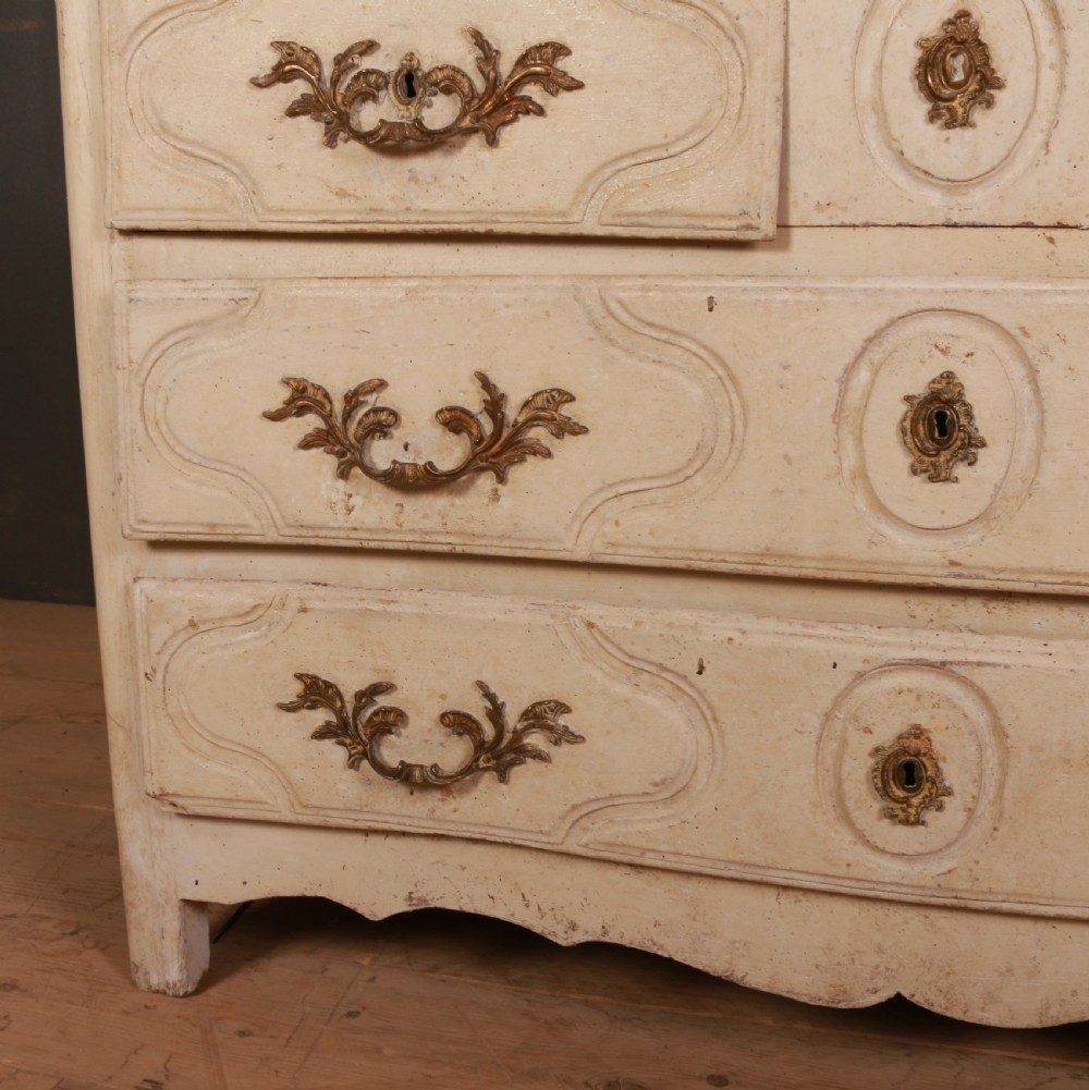 An off-white painted wooden French commode featuring three drawers with ornamental brass handles and a scalloped bottom apron. View IV