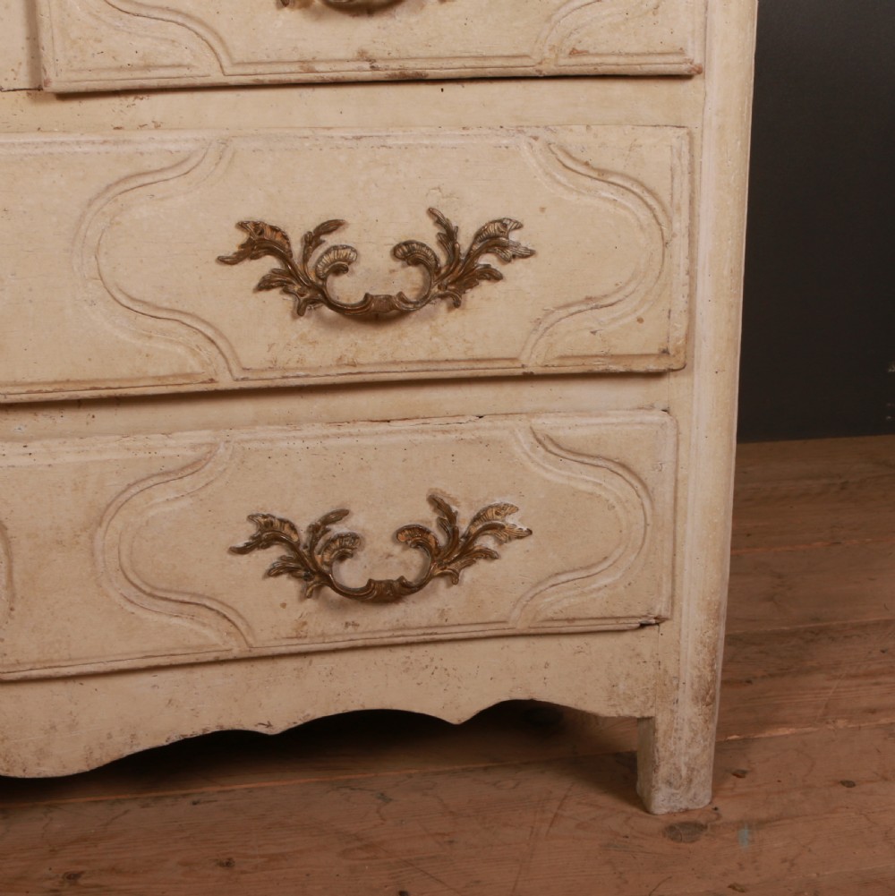 An off-white painted wooden French commode featuring three drawers with ornamental brass handles and a scalloped bottom apron. View V
