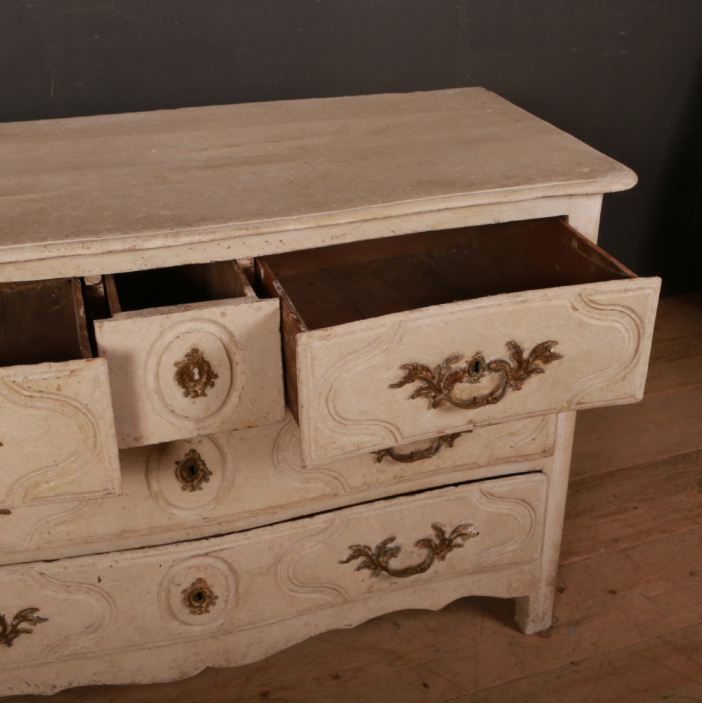 An off-white painted wooden French commode featuring three drawers with ornamental brass handles and a scalloped bottom apron. View VIII