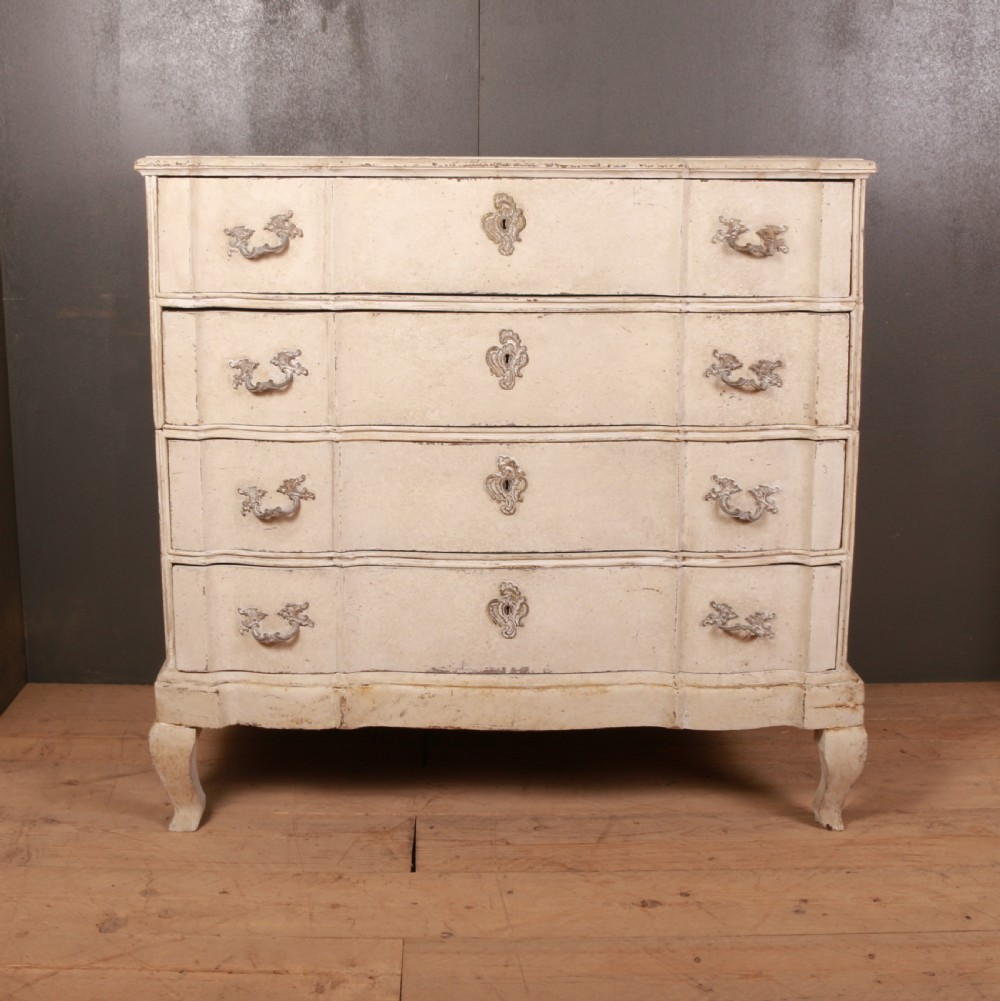 An off-white painted Danish serpentine front commode featuring four drawers with ornate hardware on short cabriole legs.