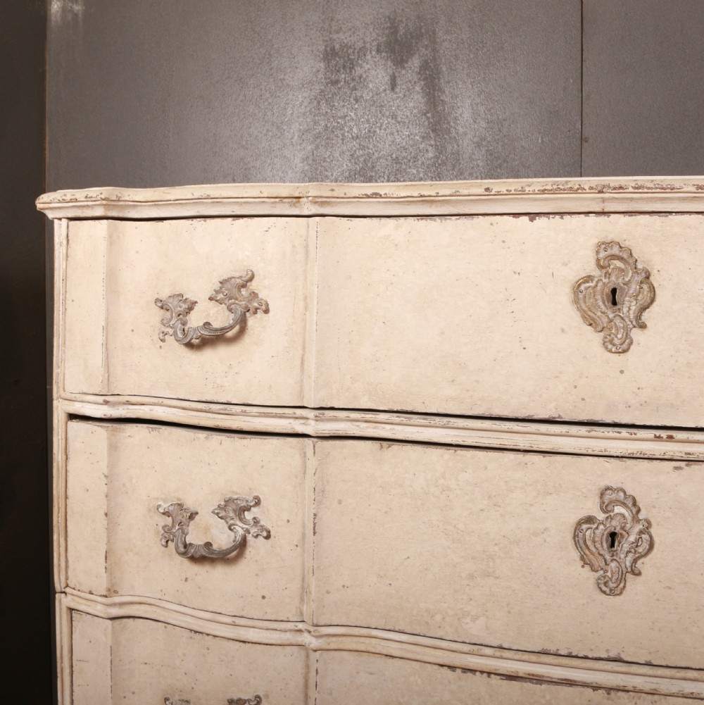 An off-white painted Danish serpentine front commode featuring four drawers with ornate hardware on short cabriole legs. View III