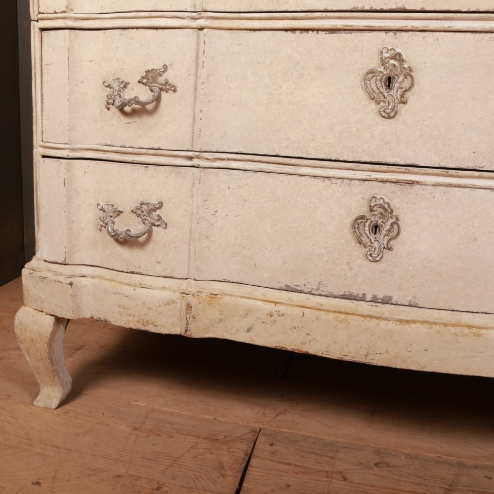 An off-white painted Danish serpentine front commode featuring four drawers with ornate hardware on short cabriole legs. View IV