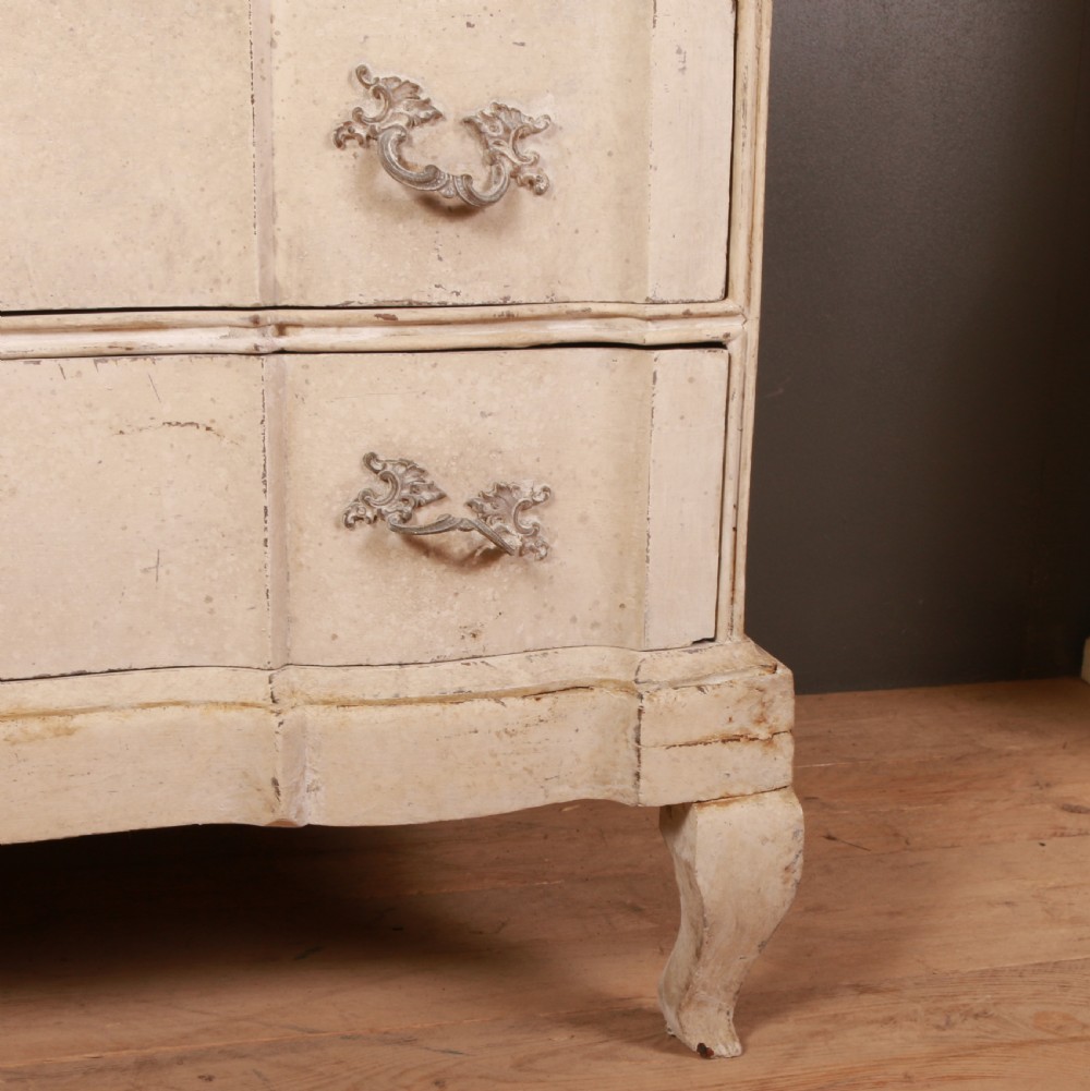 An off-white painted Danish serpentine front commode featuring four drawers with ornate hardware on short cabriole legs. View V