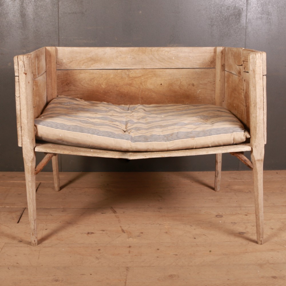 An elevated rustic wooden dog bed with three high panelled sides, straight legs, and a striped fabric cushion.