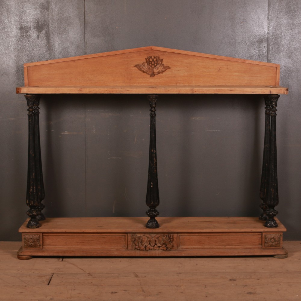 An antique bleached oak console table featuring a pediment backboard with a central carved motif, dark ebonised turned columns, and a carved lower plinth.