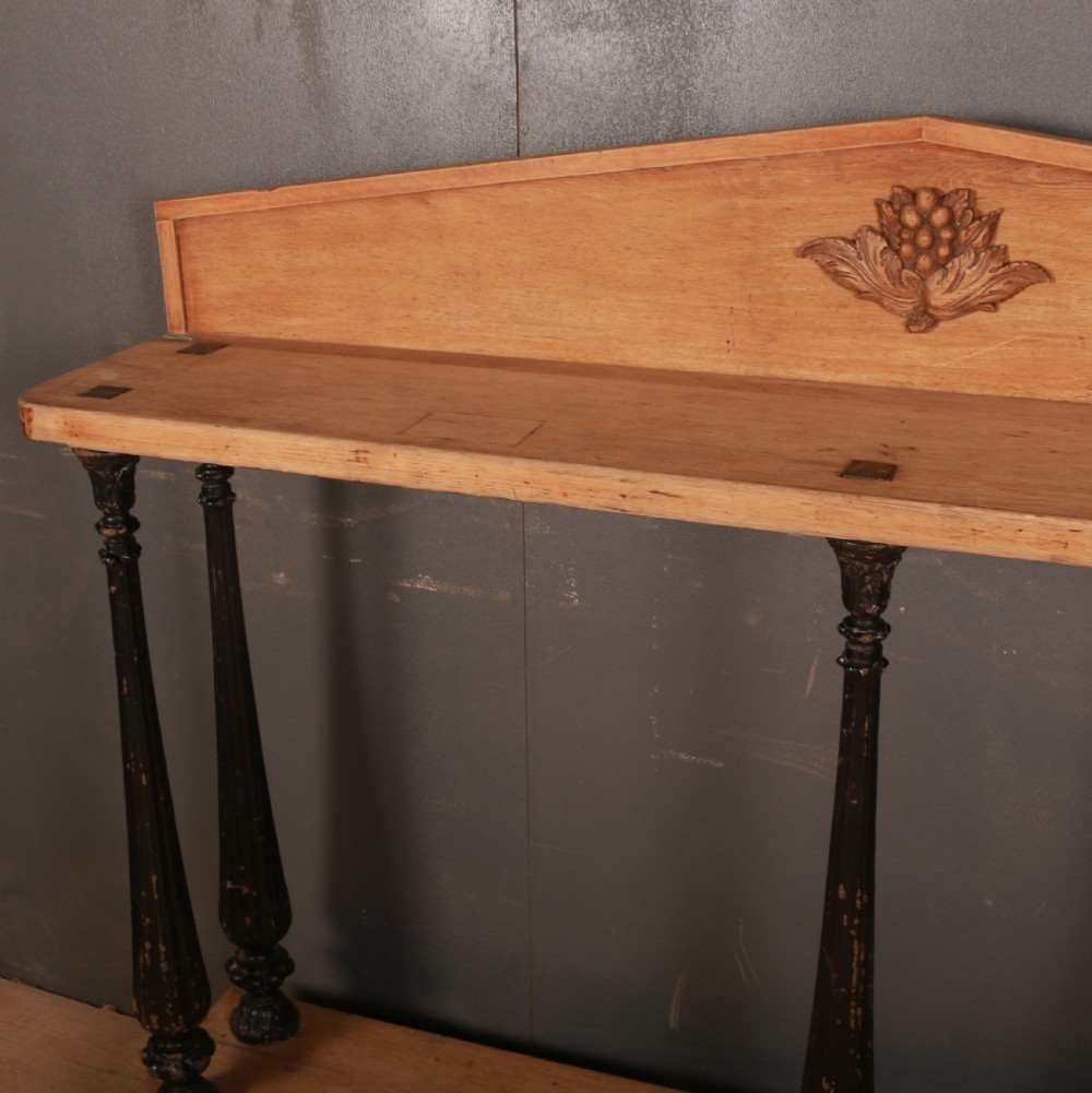 An antique bleached oak console table featuring a pediment backboard with a central carved motif, dark ebonised turned columns, and a carved lower plinth. View VIII