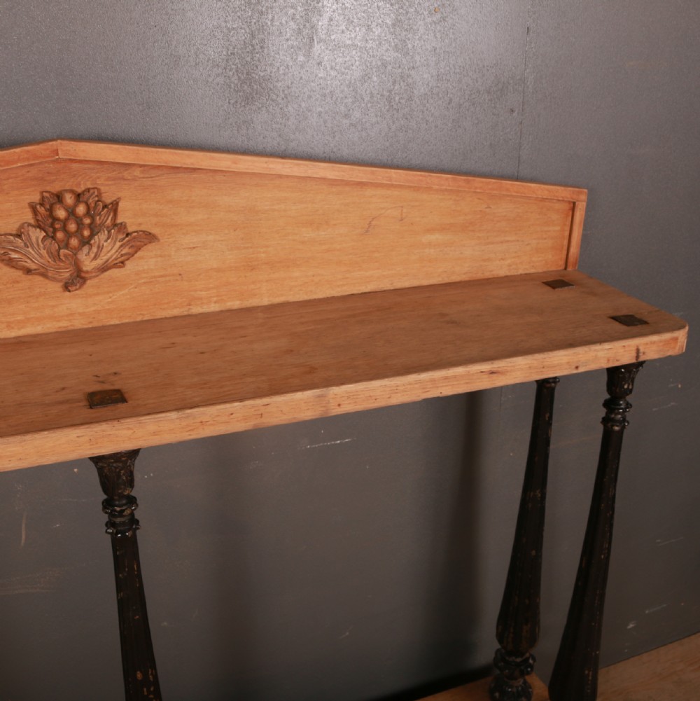 An antique bleached oak console table featuring a pediment backboard with a central carved motif, dark ebonised turned columns, and a carved lower plinth. View IX
