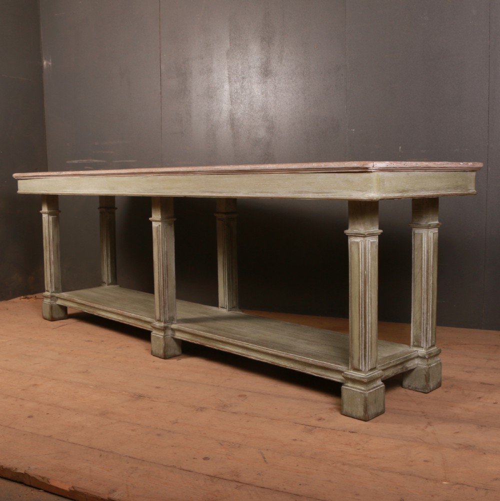 A long French drapers table featuring a muted sage green painted frame with six fluted legs, a lower full-length shelf, and a light natural timber plank top. View II