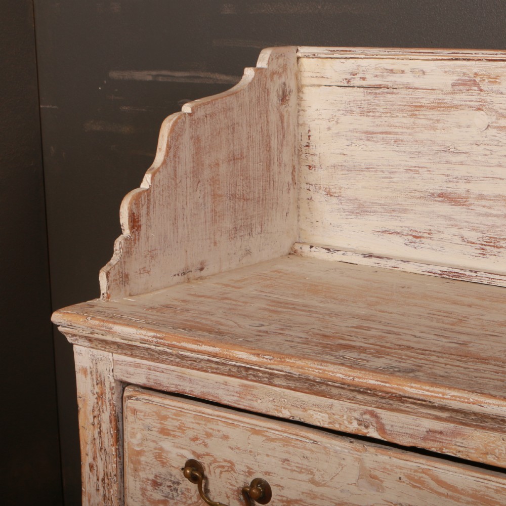 A George II painted pine dresser base with three drawers, brass drop handles, a low gallery back, and a distressed off-white finish. View III