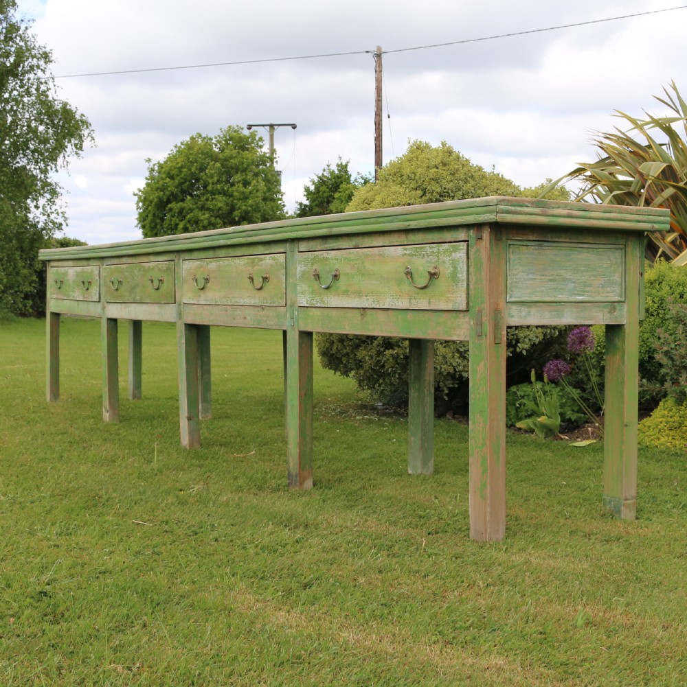 An exceptionally long antique English dresser base featuring a distressed green painted finish, multiple drawers with drop handles, and square legs.