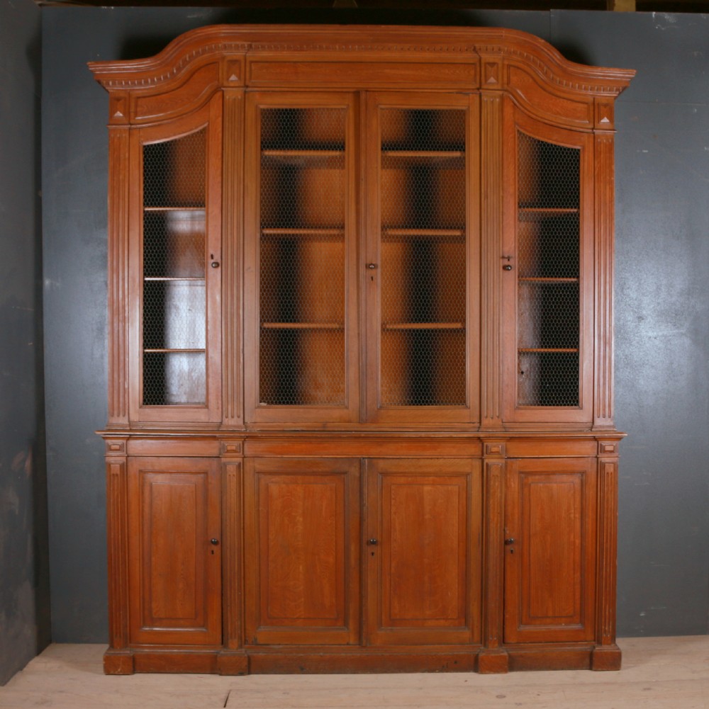 A large antique French oak bookcase with four wire mesh upper doors and four panelled lower doors featuring a shaped moulded cornice.