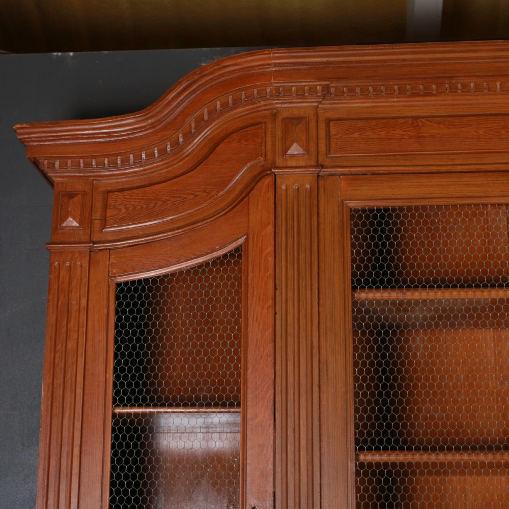 A large antique French oak bookcase with four wire mesh upper doors and four panelled lower doors featuring a shaped moulded cornice. View II
