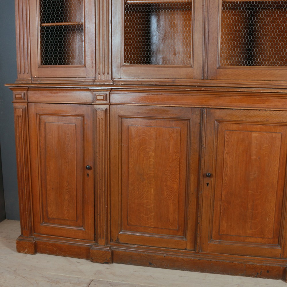 A large antique French oak bookcase with four wire mesh upper doors and four panelled lower doors featuring a shaped moulded cornice. View III