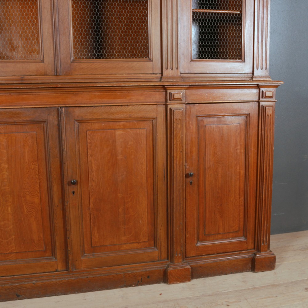 A large antique French oak bookcase with four wire mesh upper doors and four panelled lower doors featuring a shaped moulded cornice. View IV