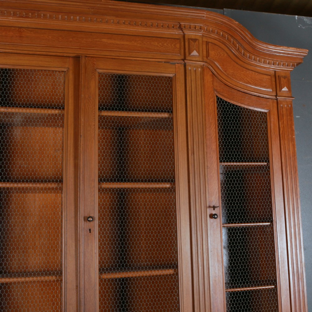 A large antique French oak bookcase with four wire mesh upper doors and four panelled lower doors featuring a shaped moulded cornice. View V