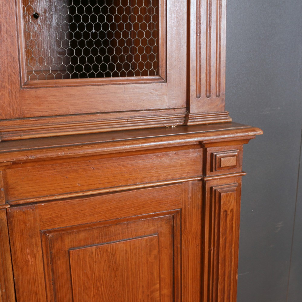 A large antique French oak bookcase with four wire mesh upper doors and four panelled lower doors featuring a shaped moulded cornice. View VI