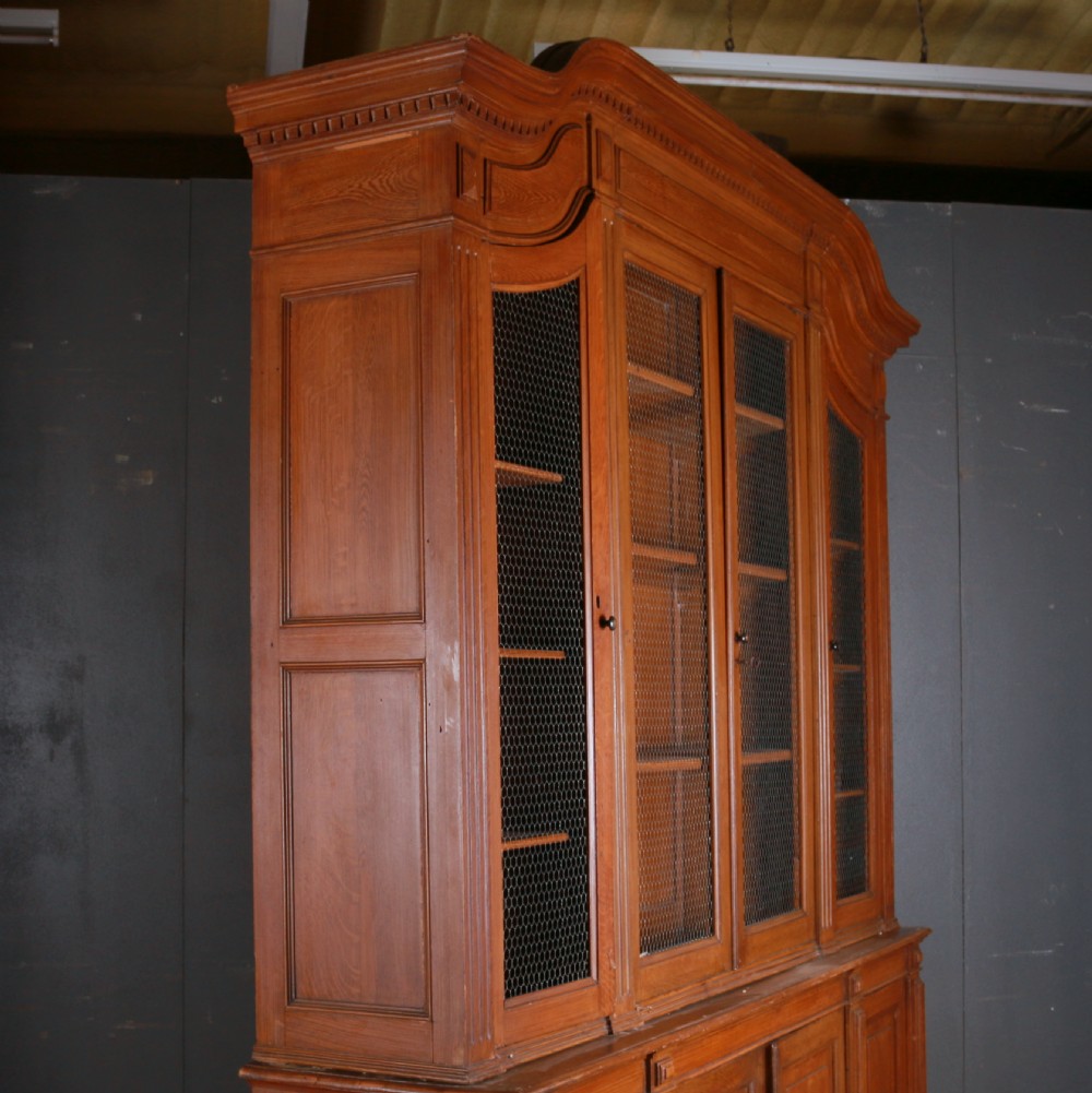 A large antique French oak bookcase with four wire mesh upper doors and four panelled lower doors featuring a shaped moulded cornice. View VIII