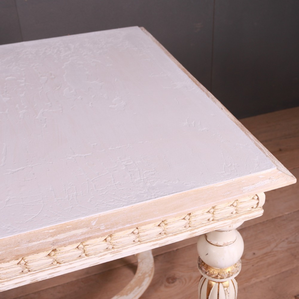 A Gustavian off-white painted lamp table featuring carved frieze detailing, gilt accents, fluted tapered legs, and a curved stretcher base. View II