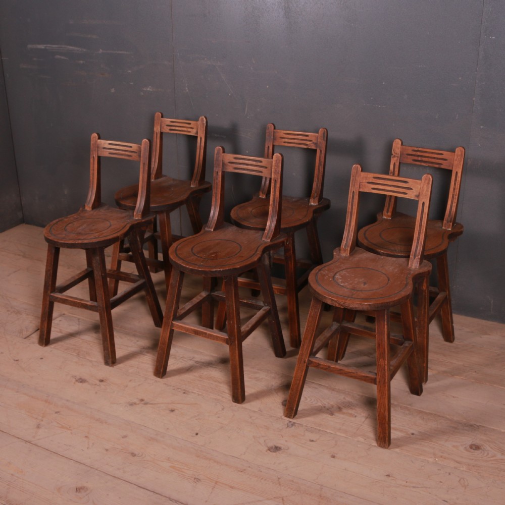 A set of six warm brown Swiss elm back stools featuring pierced top crest rails, circular carved seat details, and splayed legs with stretchers.