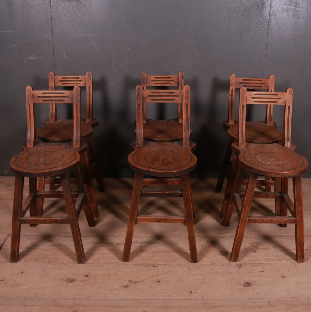 A set of six warm brown Swiss elm back stools featuring pierced top crest rails, circular carved seat details, and splayed legs with stretchers. View II